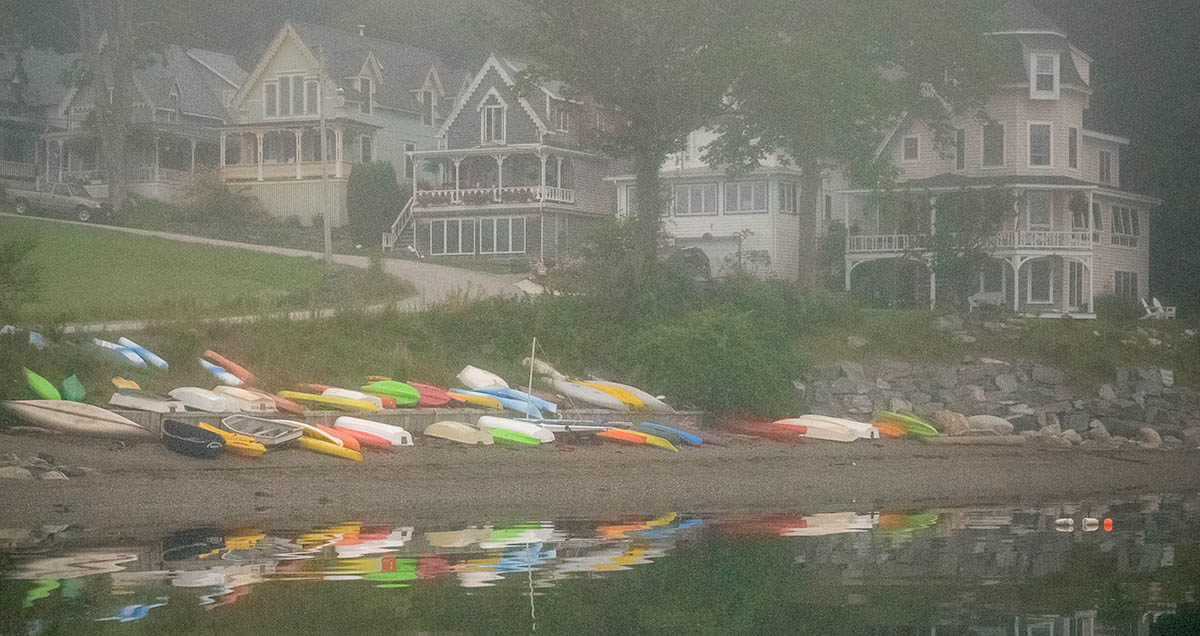 colorful kayaks rest on beach below row of victorian cottages on a foggy morning